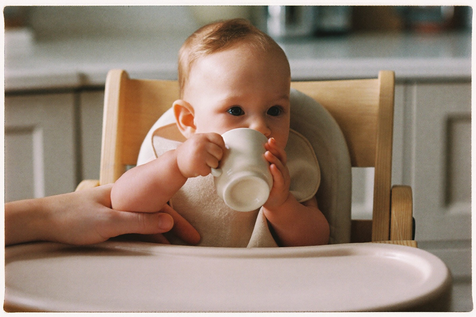 Bebé de un año bebiendo de una taza pequeña sin tapa que un adulto sostiene frente a él