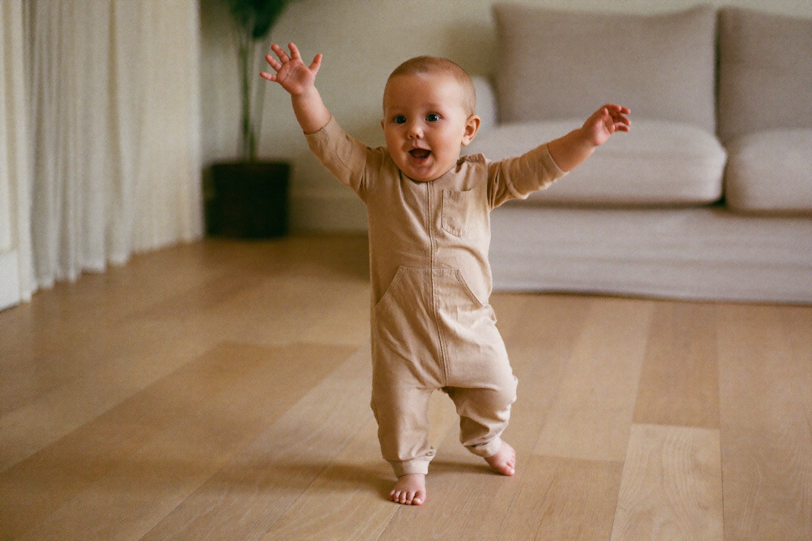 Niño de quince meses dando sus primeros pasos solo sobre un piso de madera, con los brazos separados del cuerpo