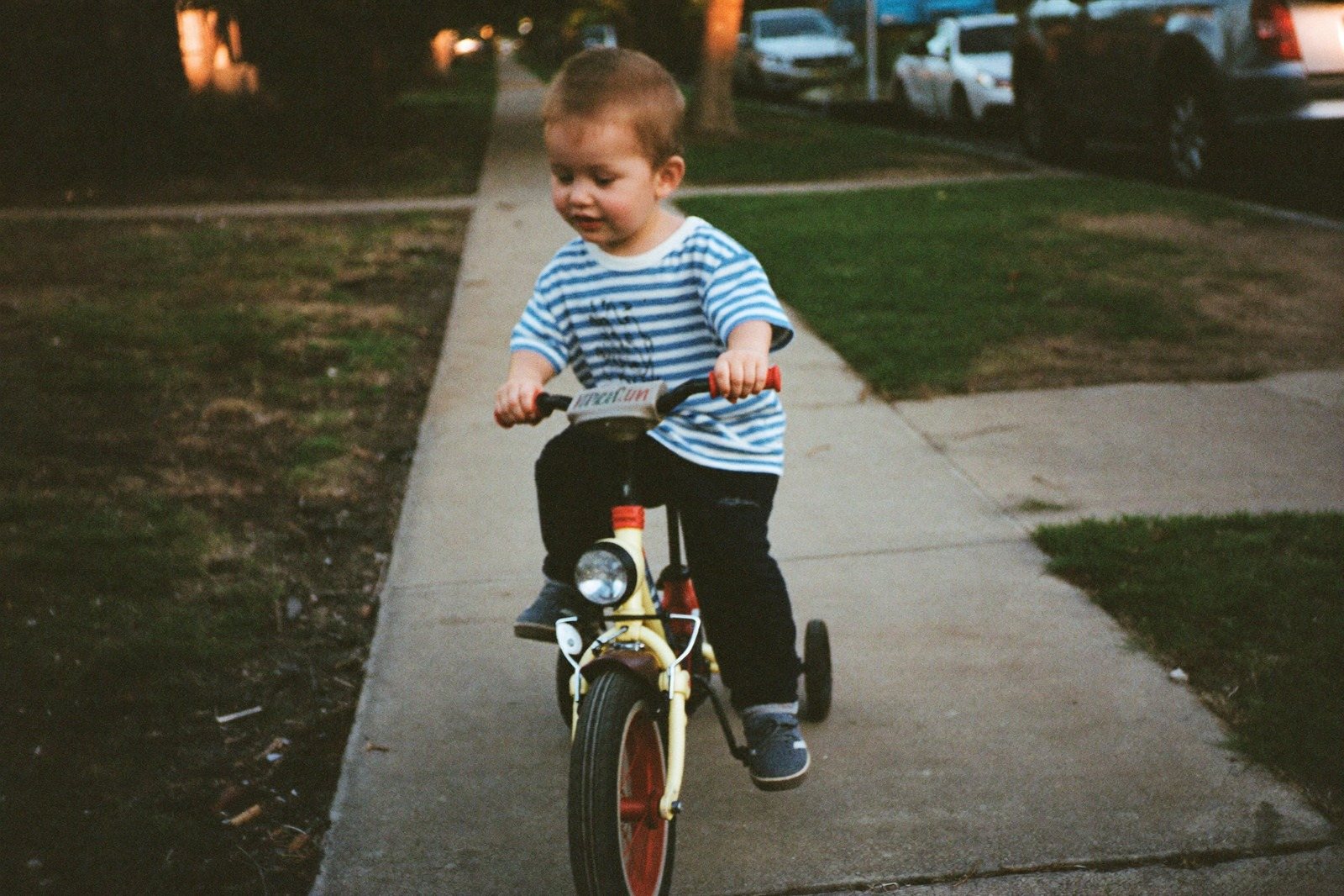 Niño de tres años pedaleando un triciclo por el camino de un parque