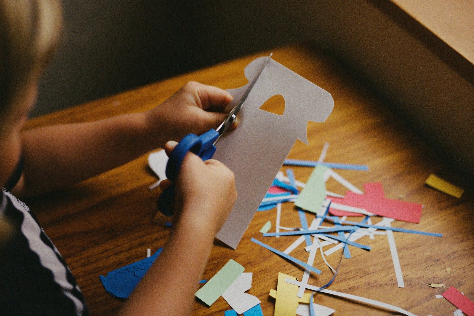Manos de un niño recortando papel de colores con tijeras sobre la mesa