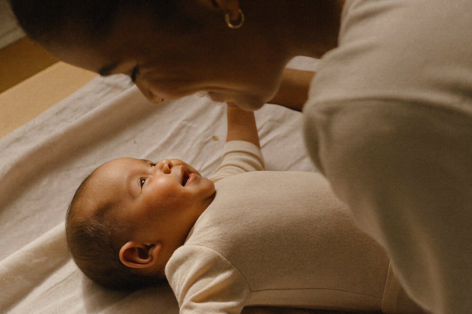 Bebé de dos meses acostado boca arriba sonriendo mientras su madre lo mira de cerca