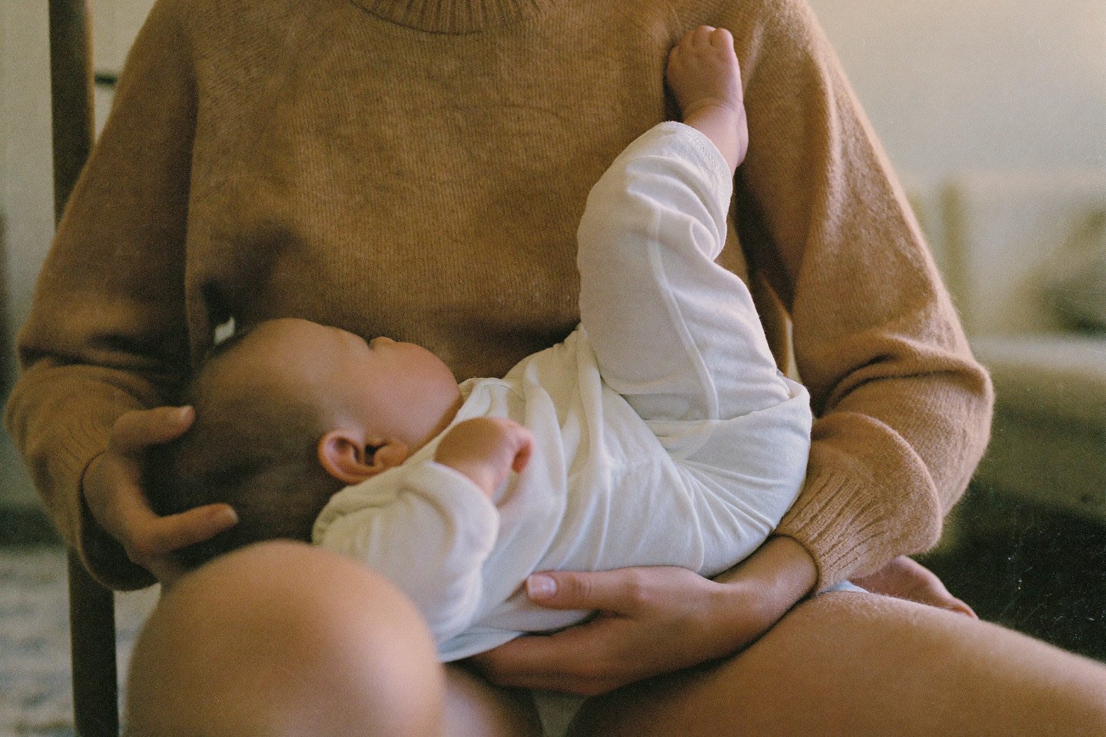 Un bebé en brazos de su mamá, recostado de lado, con la mano de ella sosteniéndole la cabeza