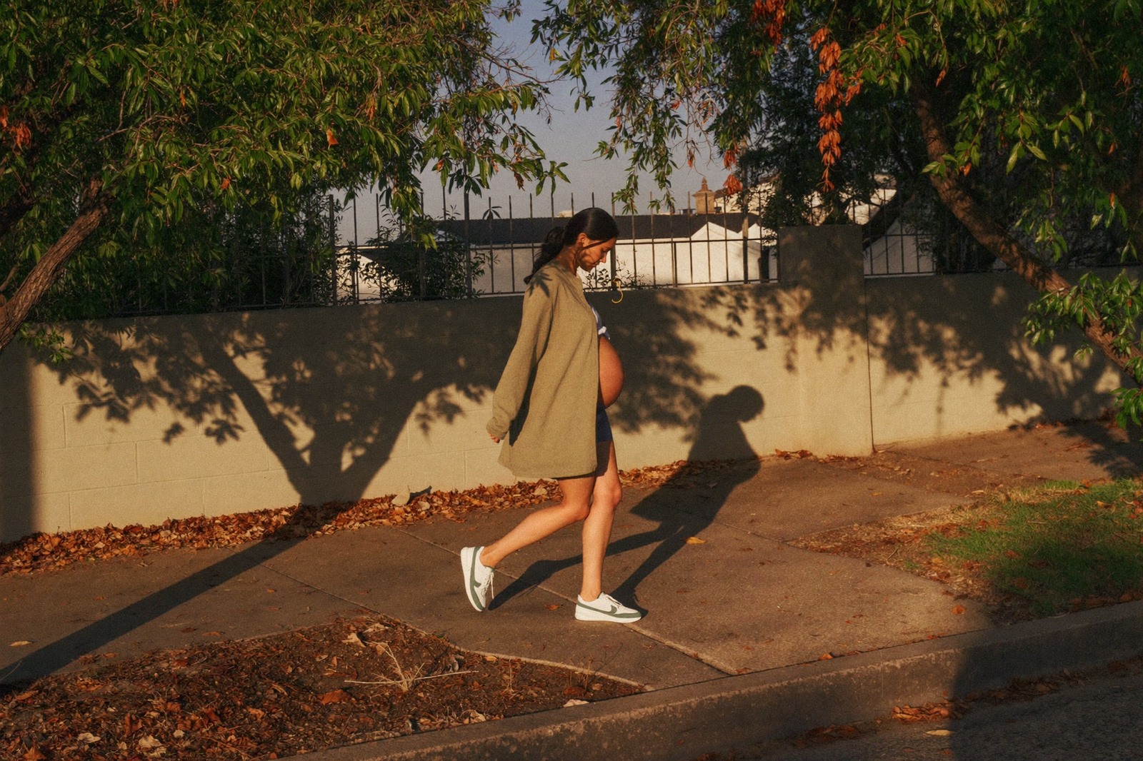 Mujer embarazada caminando por la banqueta de una calle arbolada al atardecer