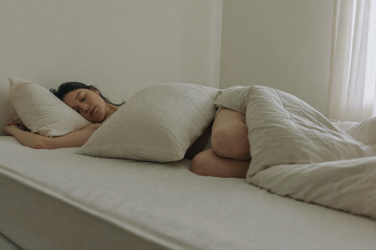 Mujer embarazada dormida de lado en su cama abrazando una almohada grande que le sostiene el vientre