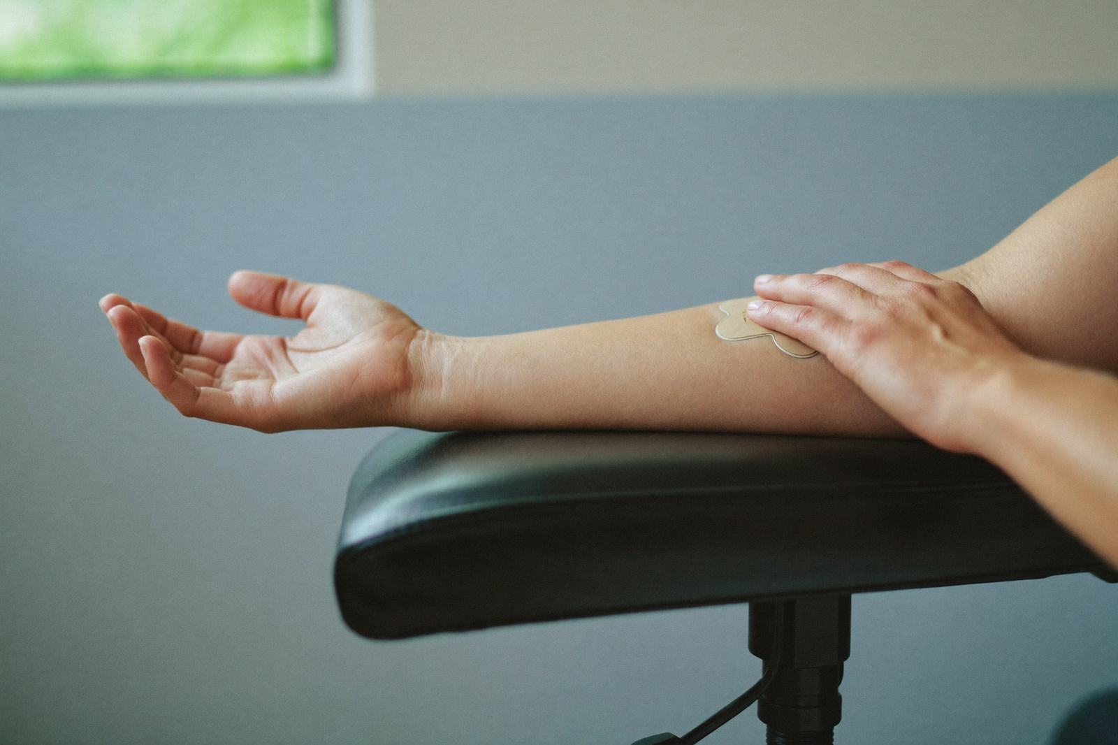 Antebrazo de una mujer con una curita en el pliegue del codo, apoyado en el brazo de un sillón de toma de muestras