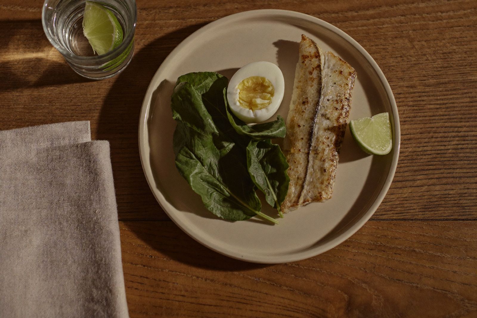 Plato con huevo, verduras de hoja verde y pescado sobre una mesa de madera junto a un vaso de agua
