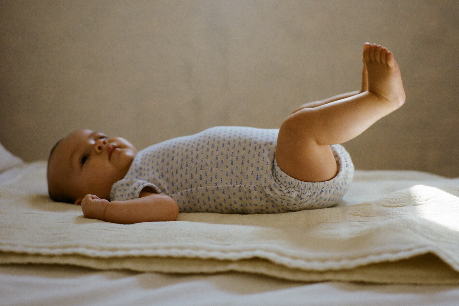 Bebé recostado boca arriba sobre una manta clara, con las piernas flexionadas