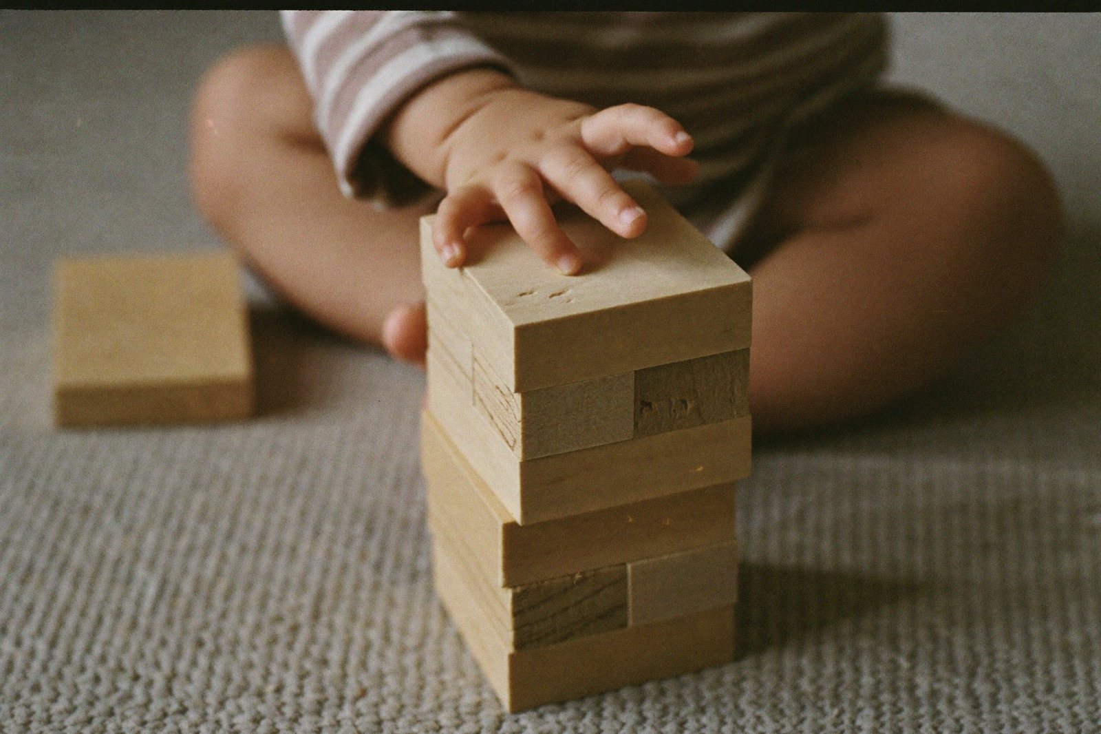 Manos de un bebé apilando dos cubos de madera sobre una alfombra