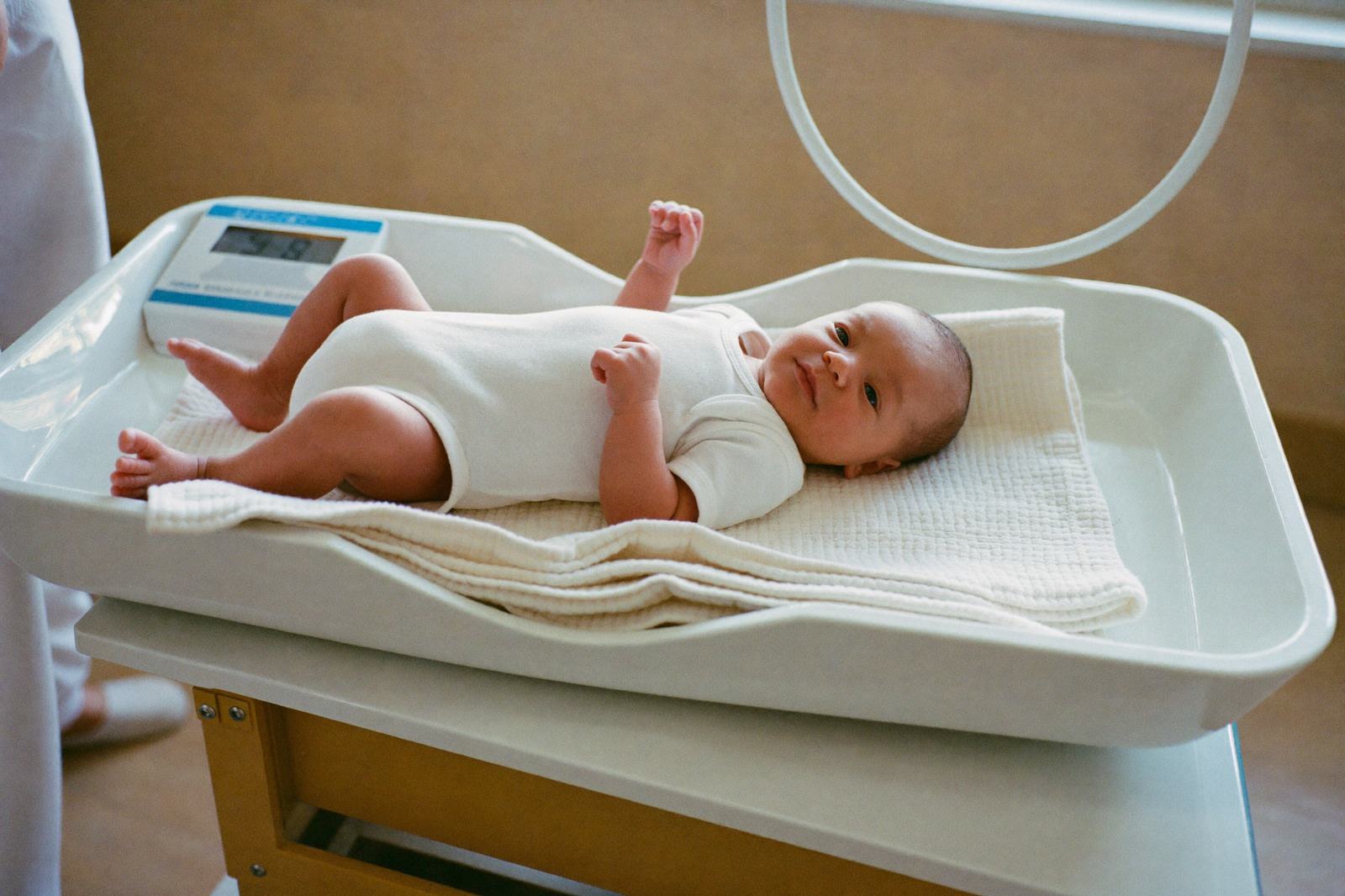 Un bebé recostado sobre una báscula pediátrica blanca en el consultorio, con una manta doblada debajo