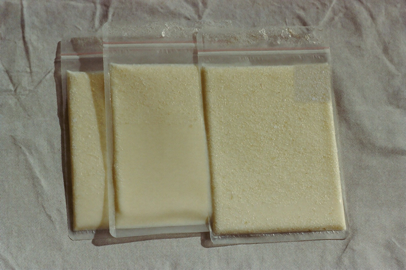 Tres bolsas planas de leche materna congelada, apiladas sobre una tela de lino claro, con escarcha en la superficie