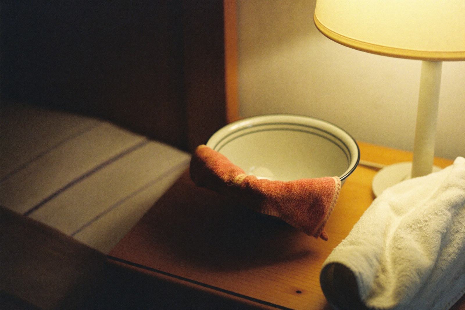 Una toalla pequeña doblada junto a un tazón con agua tibia sobre una mesa de madera