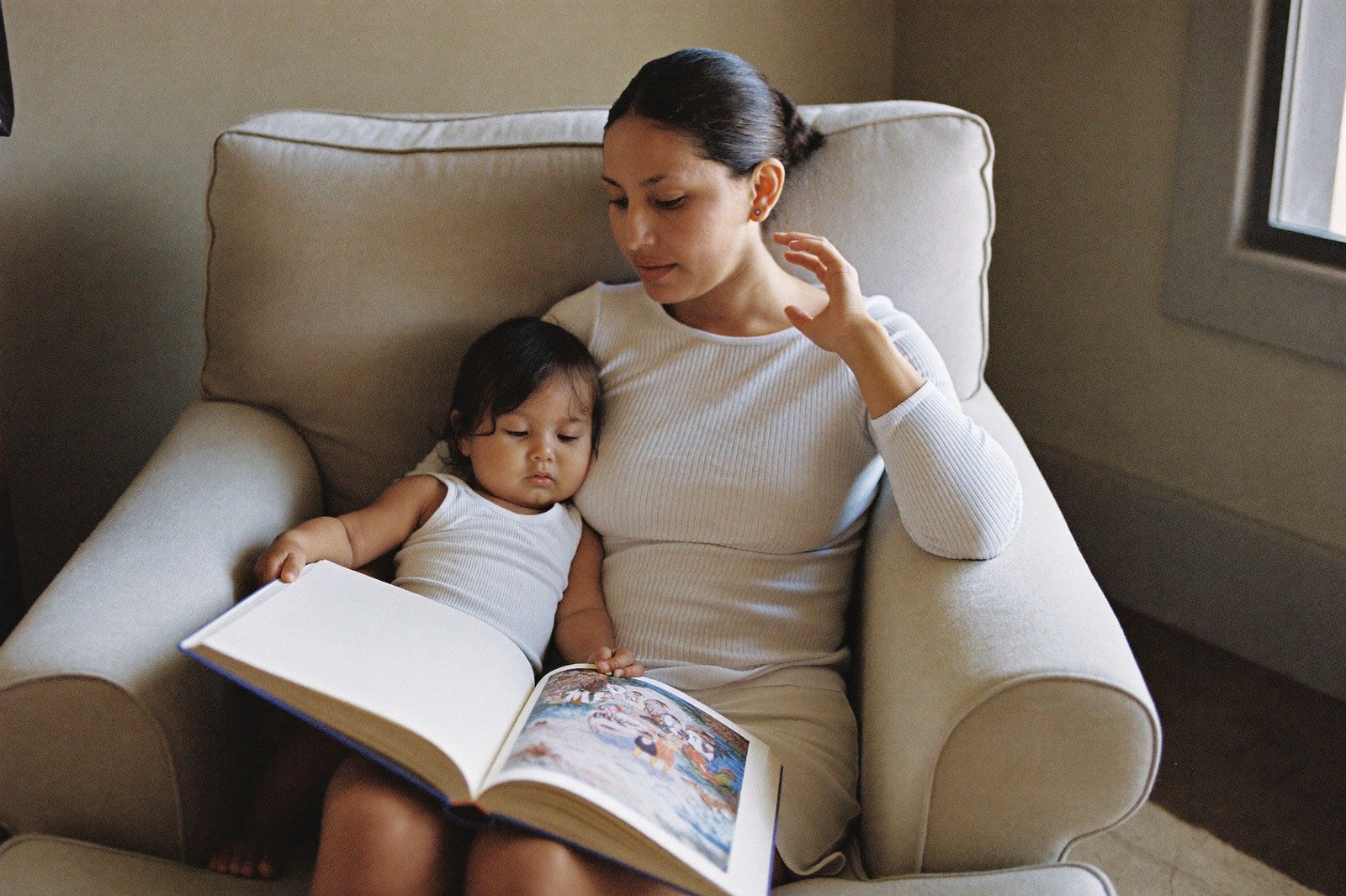 Una mamá abraza a su hijo pequeño sentada en un sillón, con un libro abierto sobre las piernas