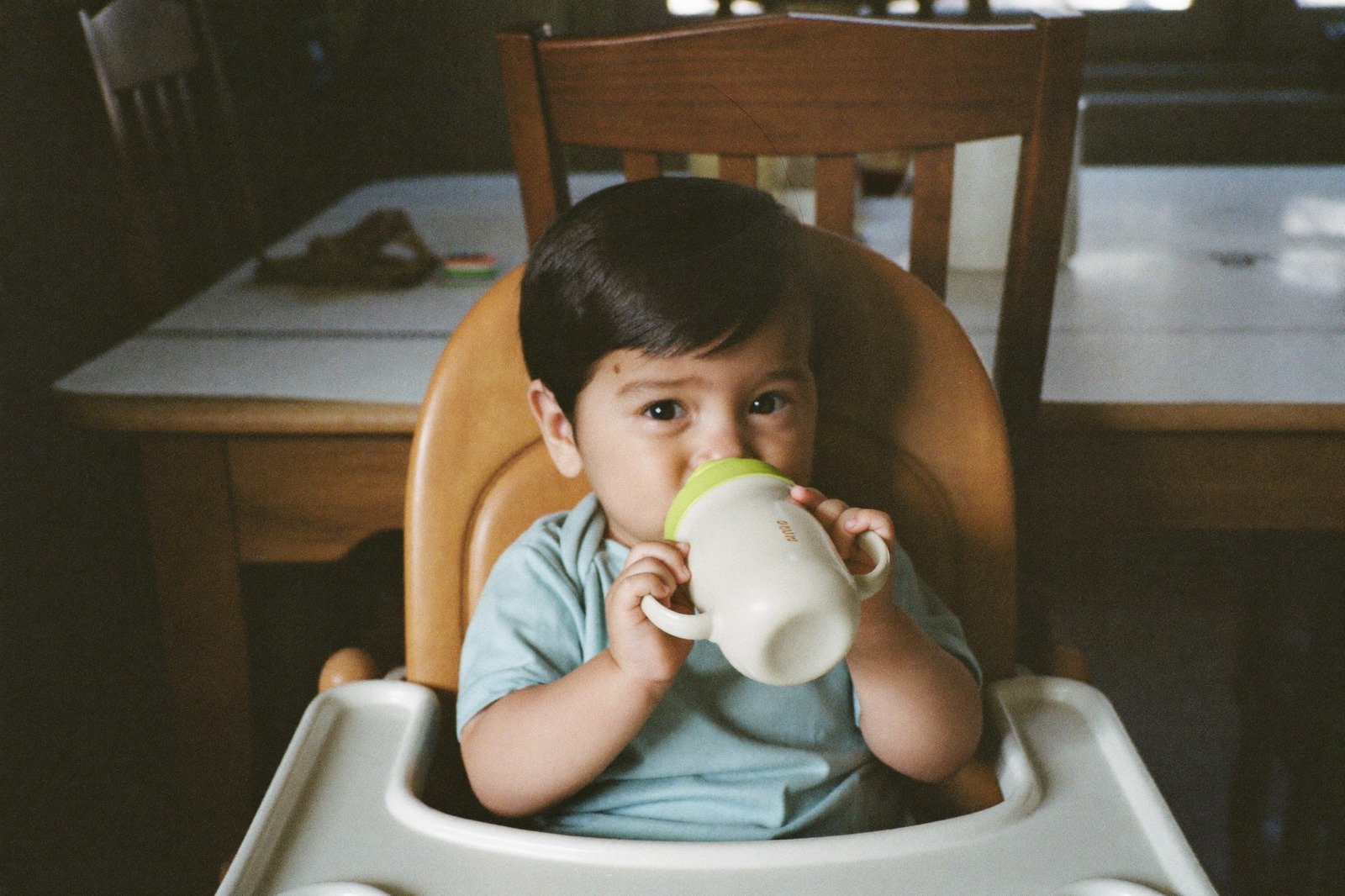 Un bebé sentado en una silla alta bebiendo de una taza de aprendizaje, con las dos manos en las asas