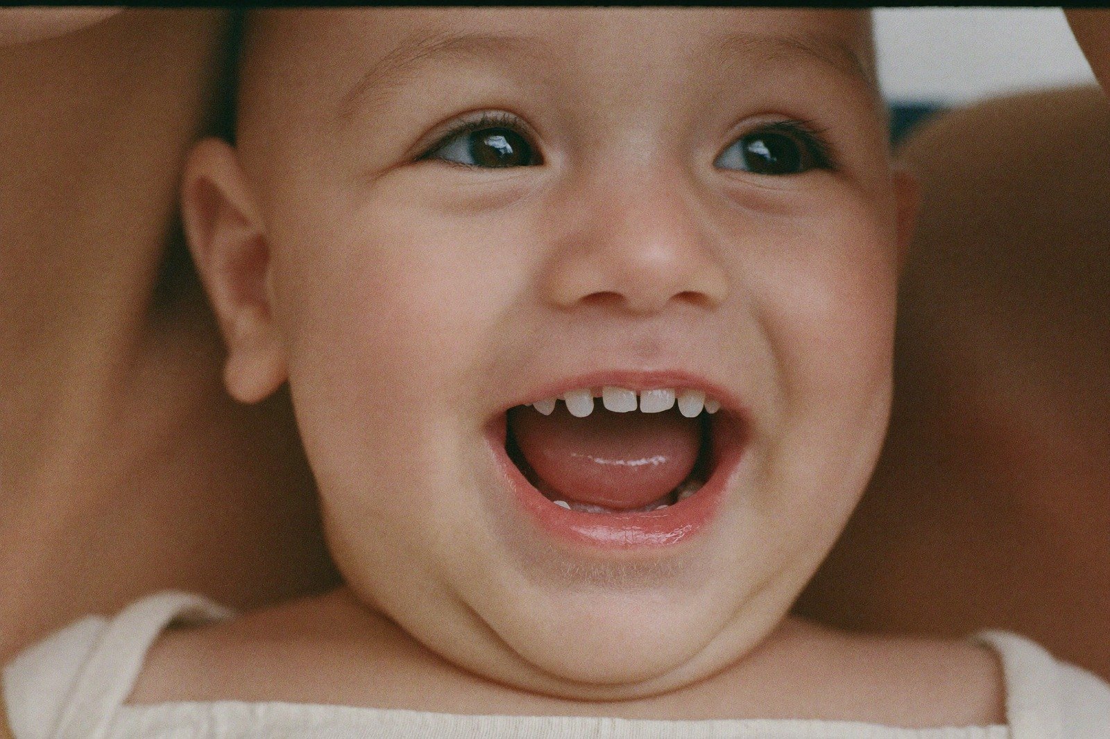 Un bebé sonriente sentado sobre una manta, mostrando sus primeros dientes inferiores