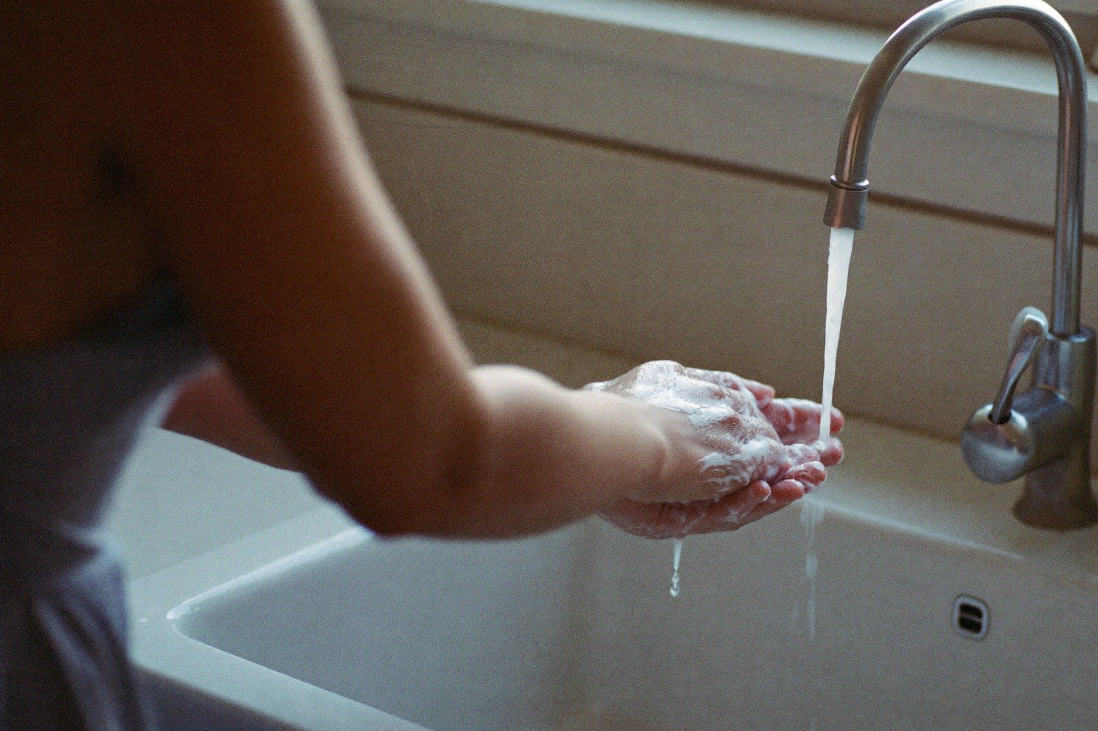 Manos enjabonadas bajo el chorro de agua en un lavabo blanco