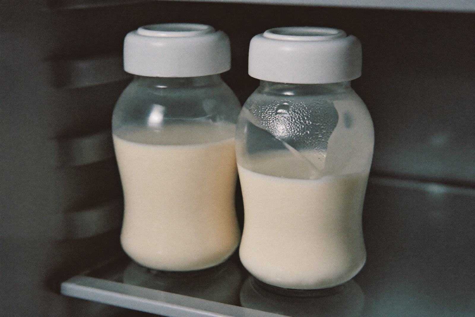 Dos frascos de vidrio con leche materna en el fondo de un estante del refrigerador, con la etiqueta fechada visible en cada uno