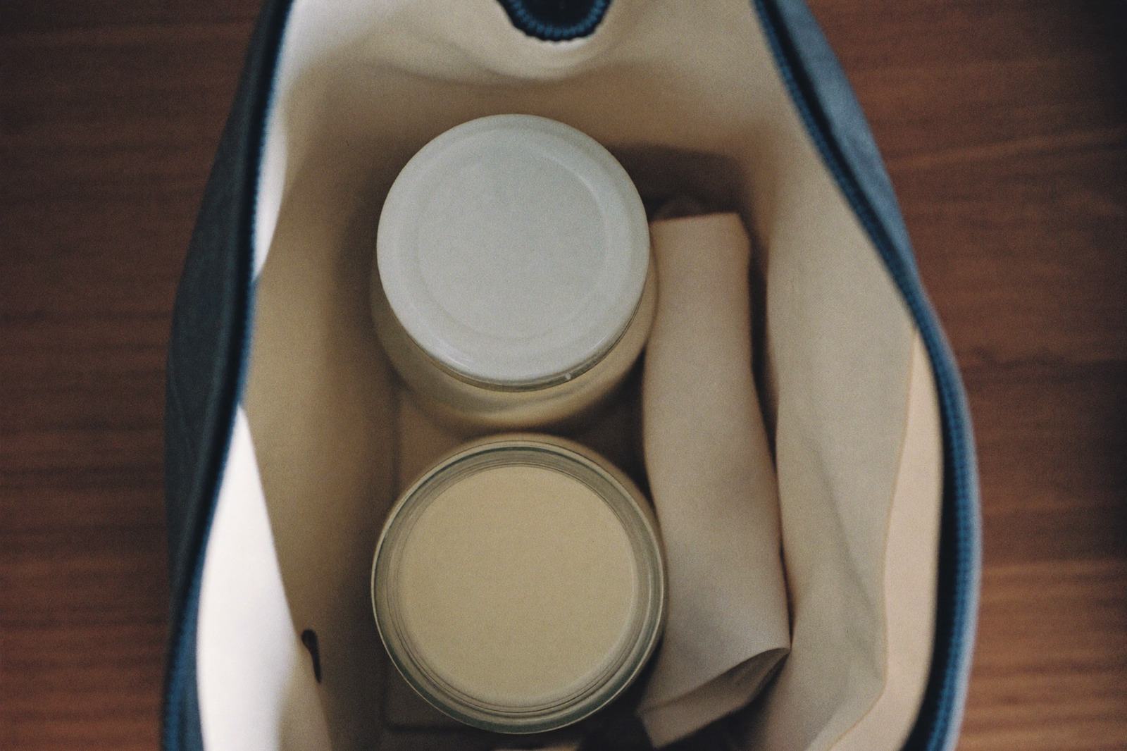 Vista desde arriba de una hielera abierta sobre un escritorio, con dos frascos de leche materna y un paño doblado