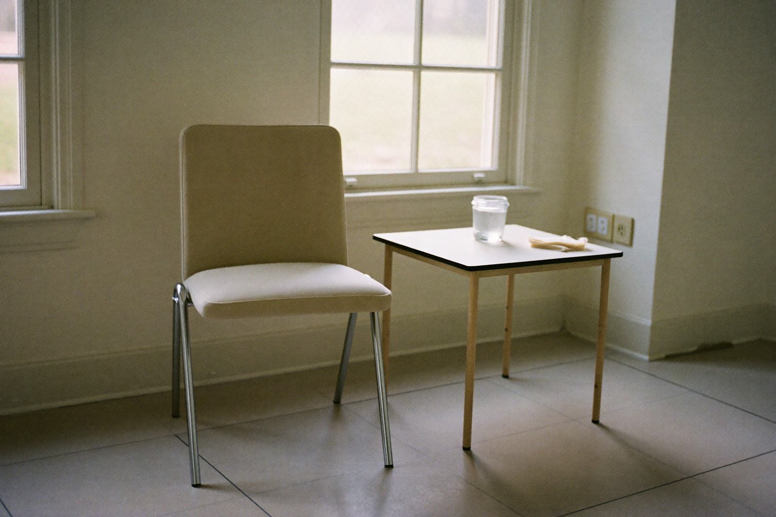 Una silla y una mesa pequeña junto a una ventana en una sala de lactancia con un frasco limpio encima