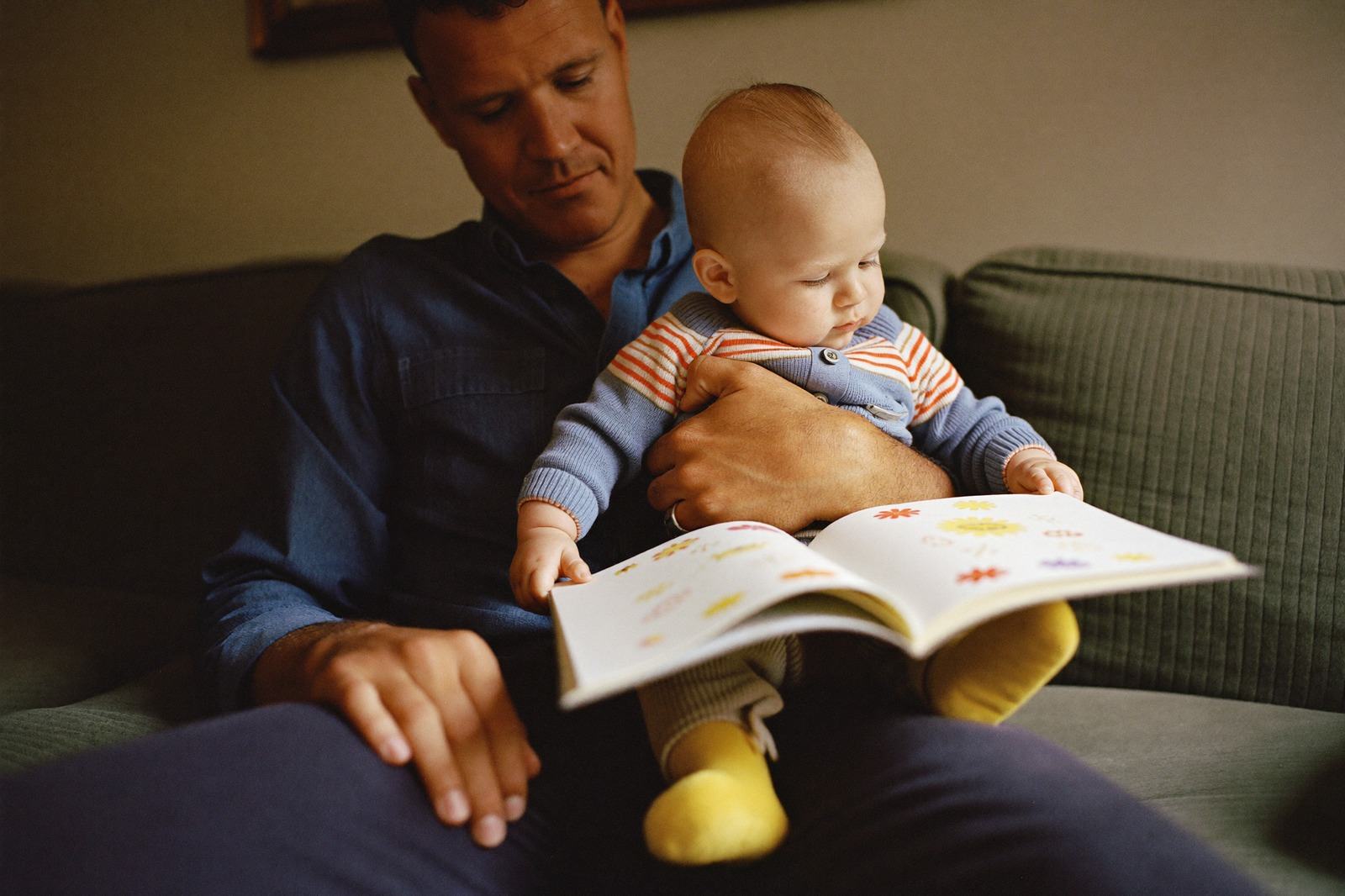 Un bebé de once meses pasando la página de un libro de tela sentado en el regazo de su padre