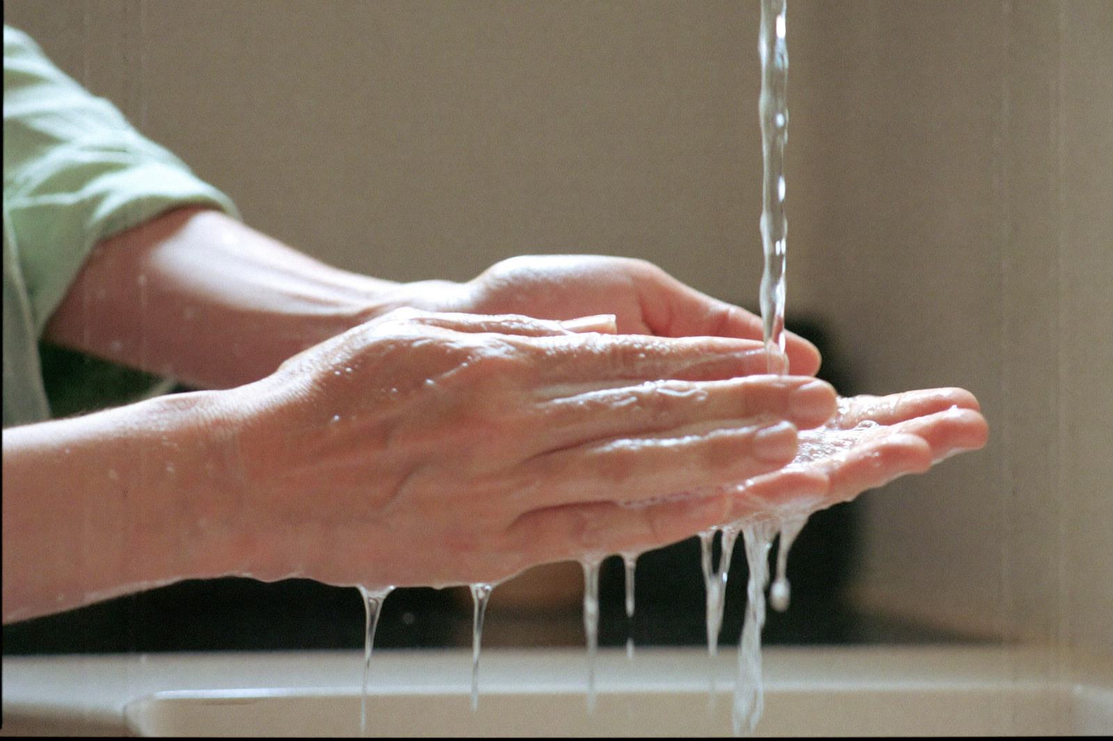 Manos de un adulto enjabonándose bajo el chorro del lavabo, con la luz de la cocina al fondo