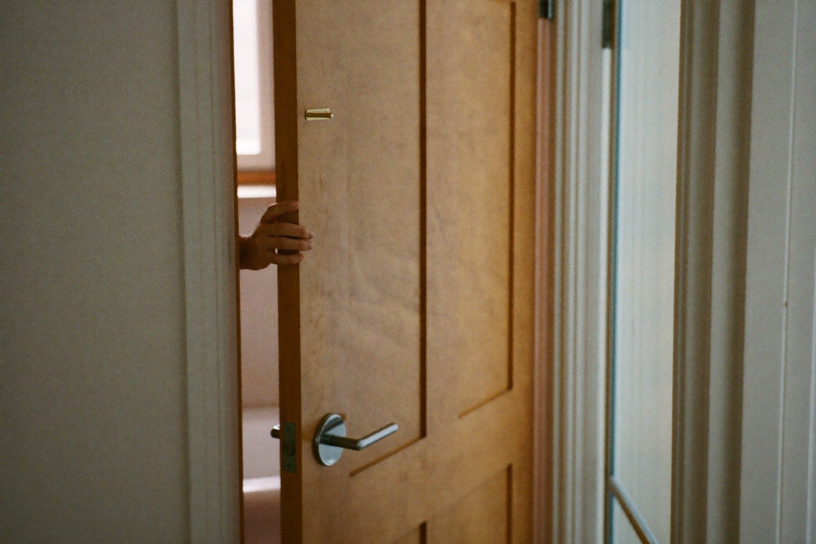 Puerta de un baño con la mano de un adulto apoyada en el marco