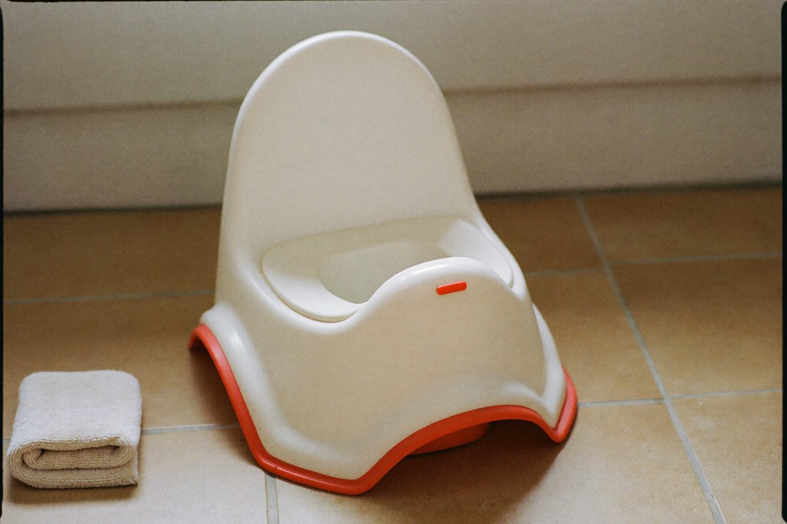 Bacinica infantil de plástico blanco sobre el piso de un baño con luz natural