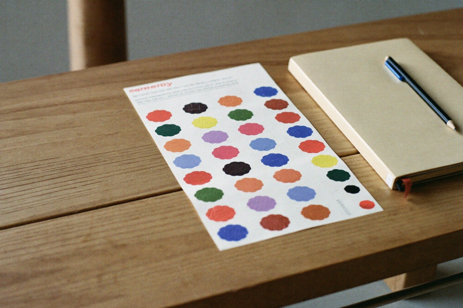 Hoja de calcomanías de colores sobre una mesa de madera junto a un cuaderno
