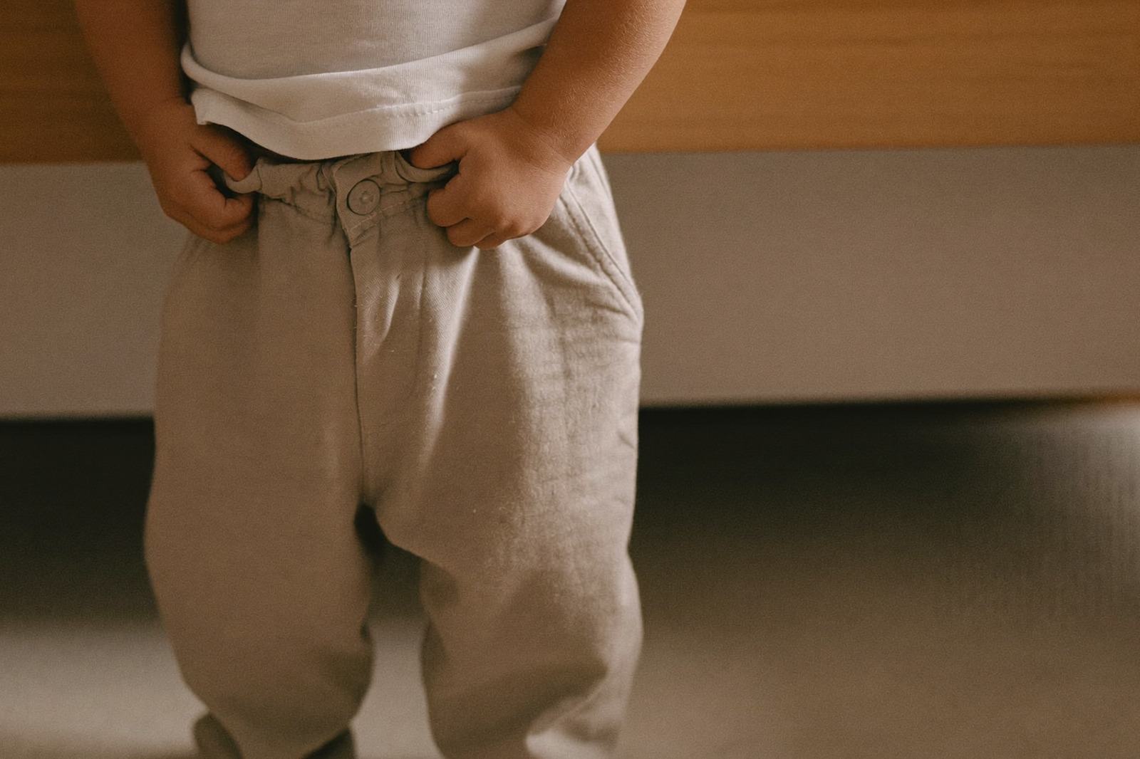 Niño pequeño de pie subiéndose un pantalón holgado en la habitación