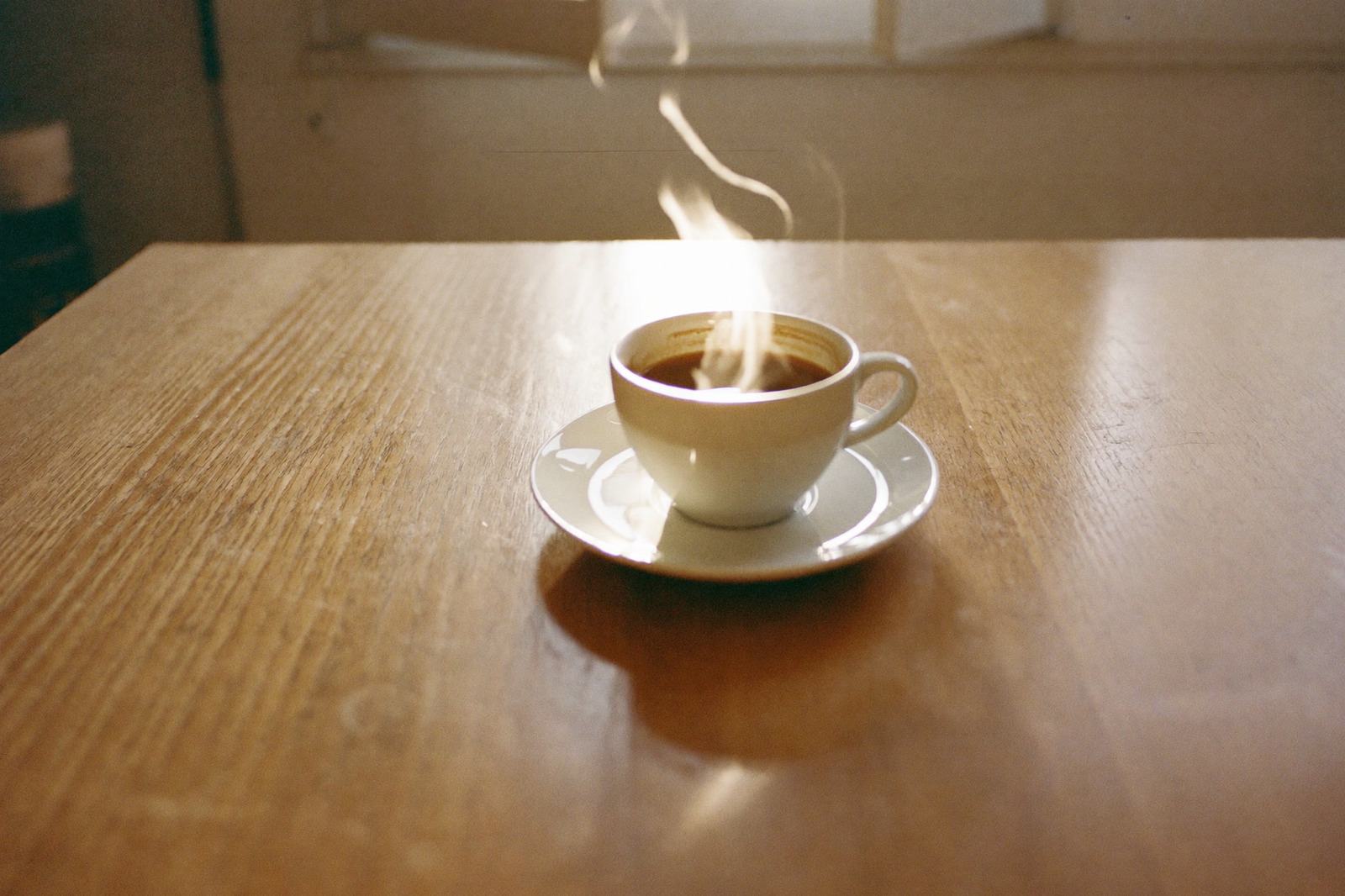 Taza de café humeante colocada al centro de una mesa de madera, lejos de la orilla, en una cocina con luz de mañana