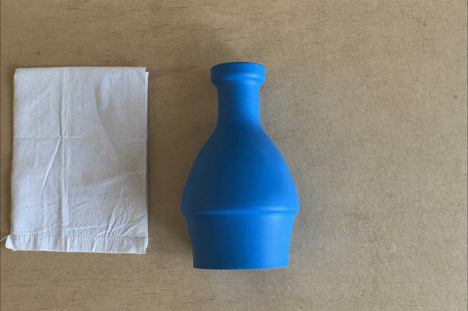 Una perilla de succión nasal de hule azul y una tela de algodón doblada sobre una superficie de madera clara, vistas desde arriba