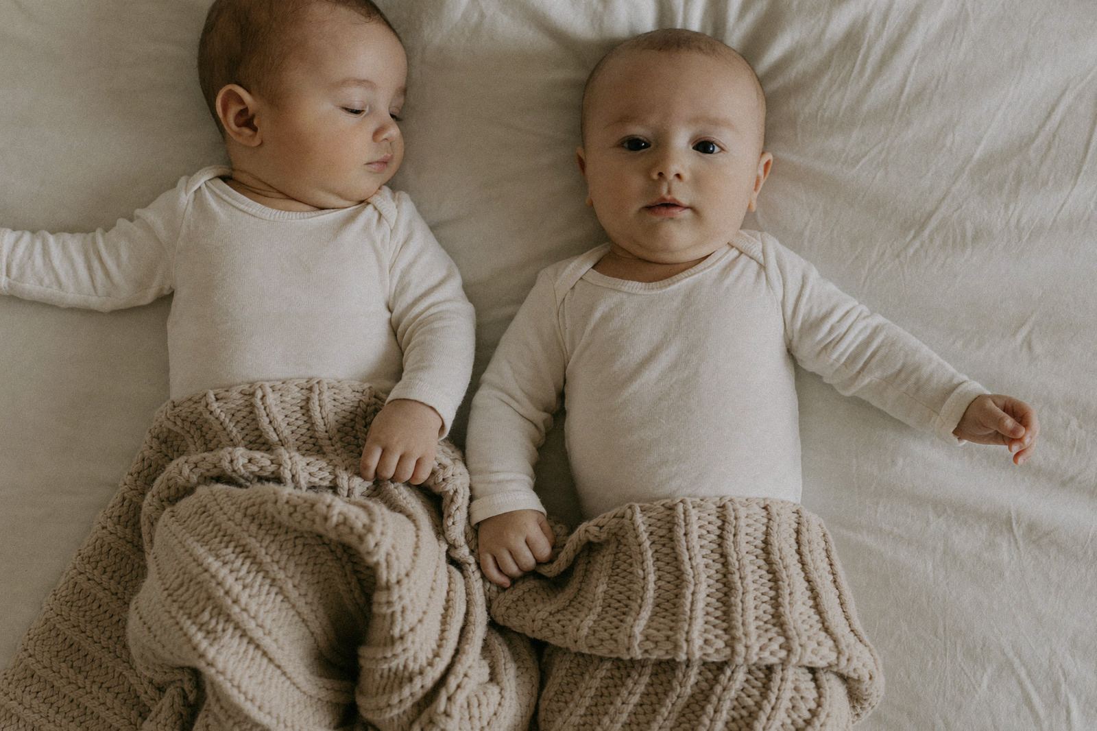 Dos bebés recién nacidos acostados uno junto al otro sobre una manta clara