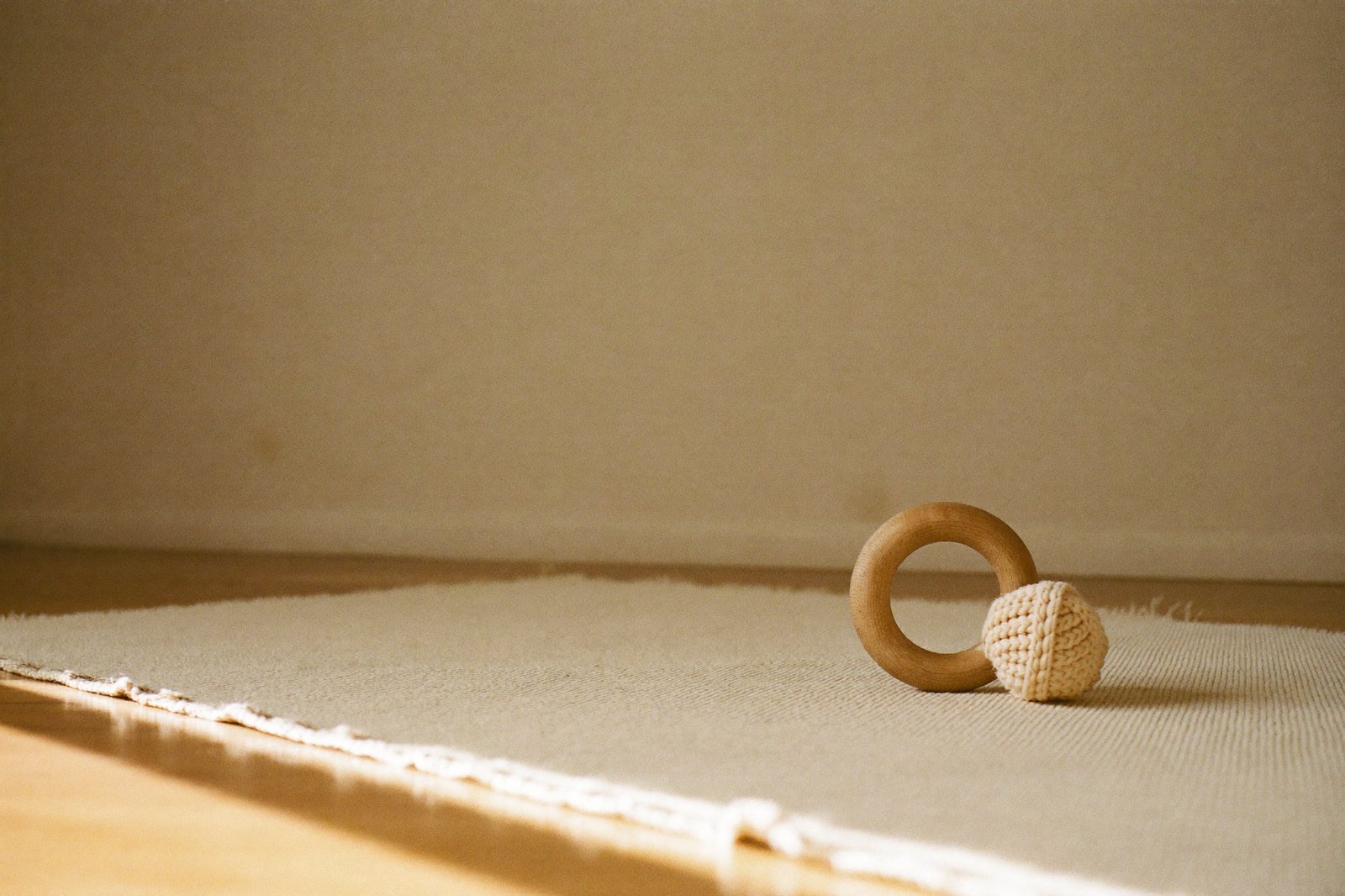 Un tapete claro en el piso de una habitación con luz de mañana, con un aro de madera y una pelota tejida encima