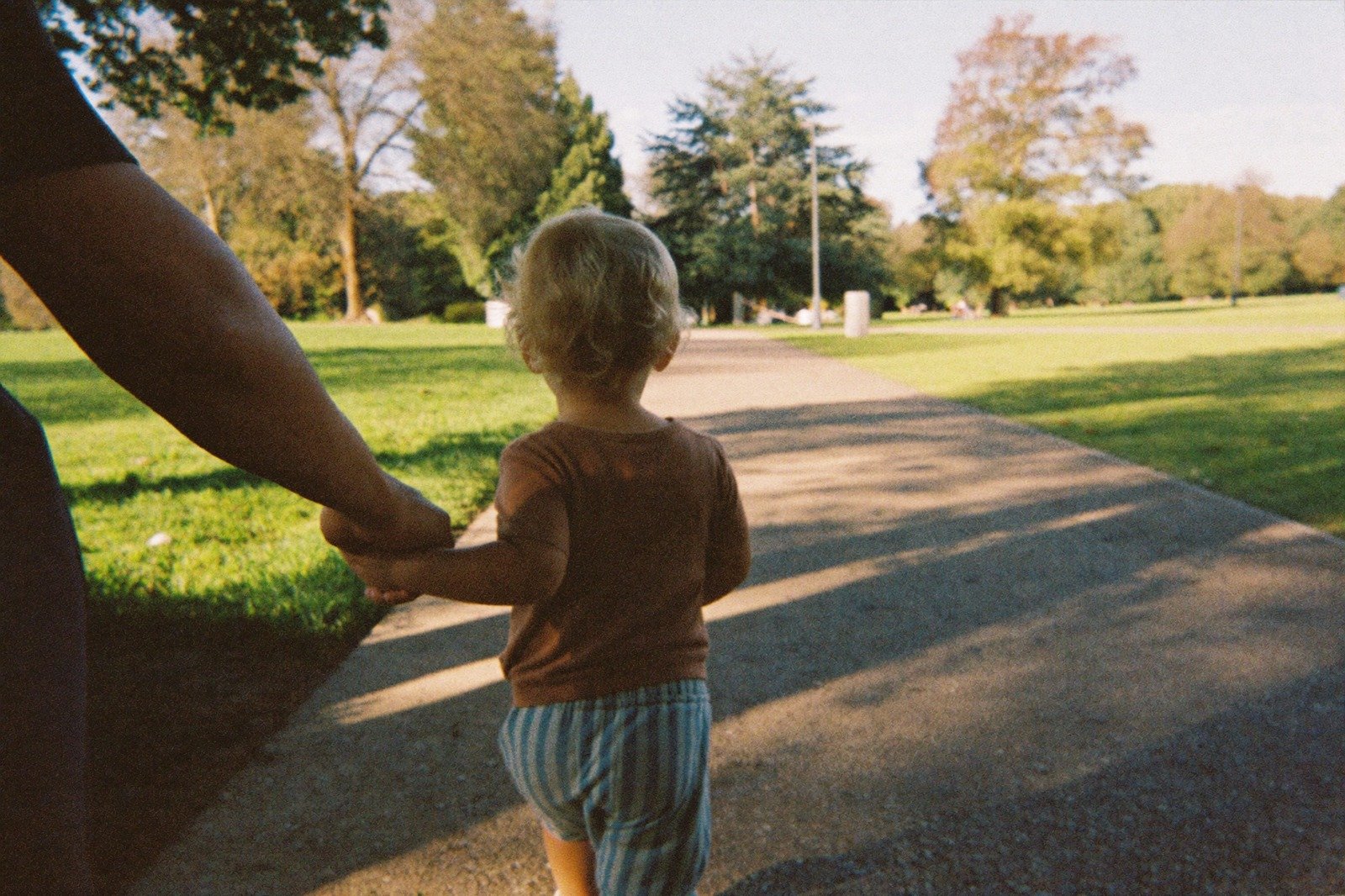 Niño pequeño caminando por un sendero de un parque acompañado de un adulto