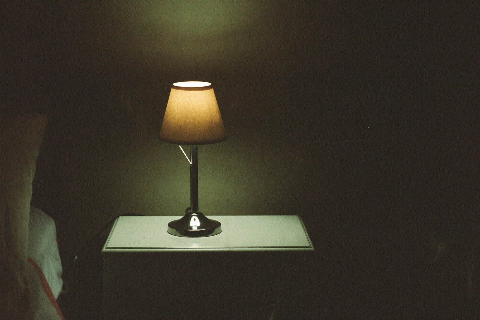 Lámpara pequeña encendida sobre una mesa de noche en una habitación a oscuras