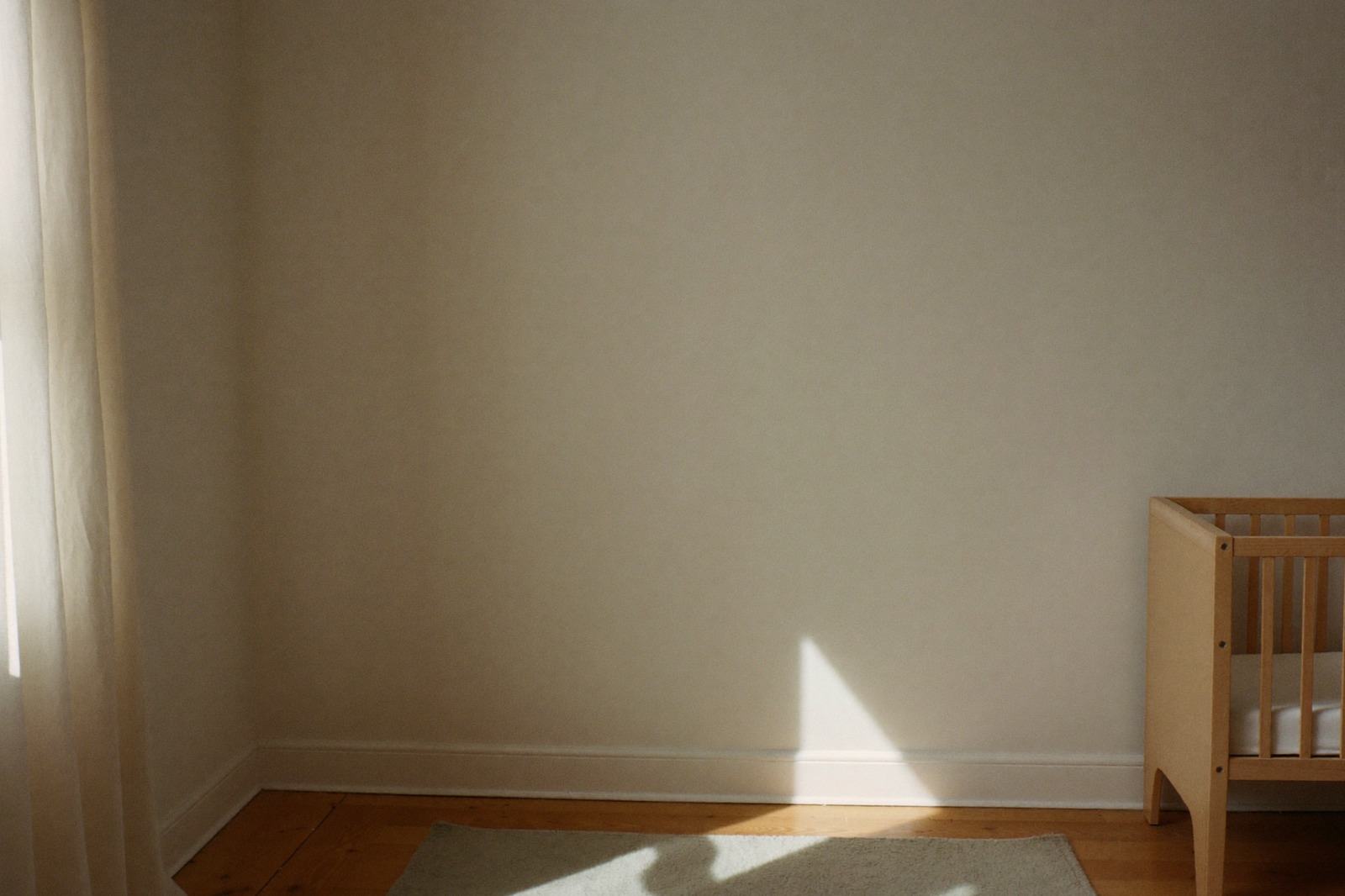 Habitación infantil con una alfombra clara y una cuna al fondo, con luz de día