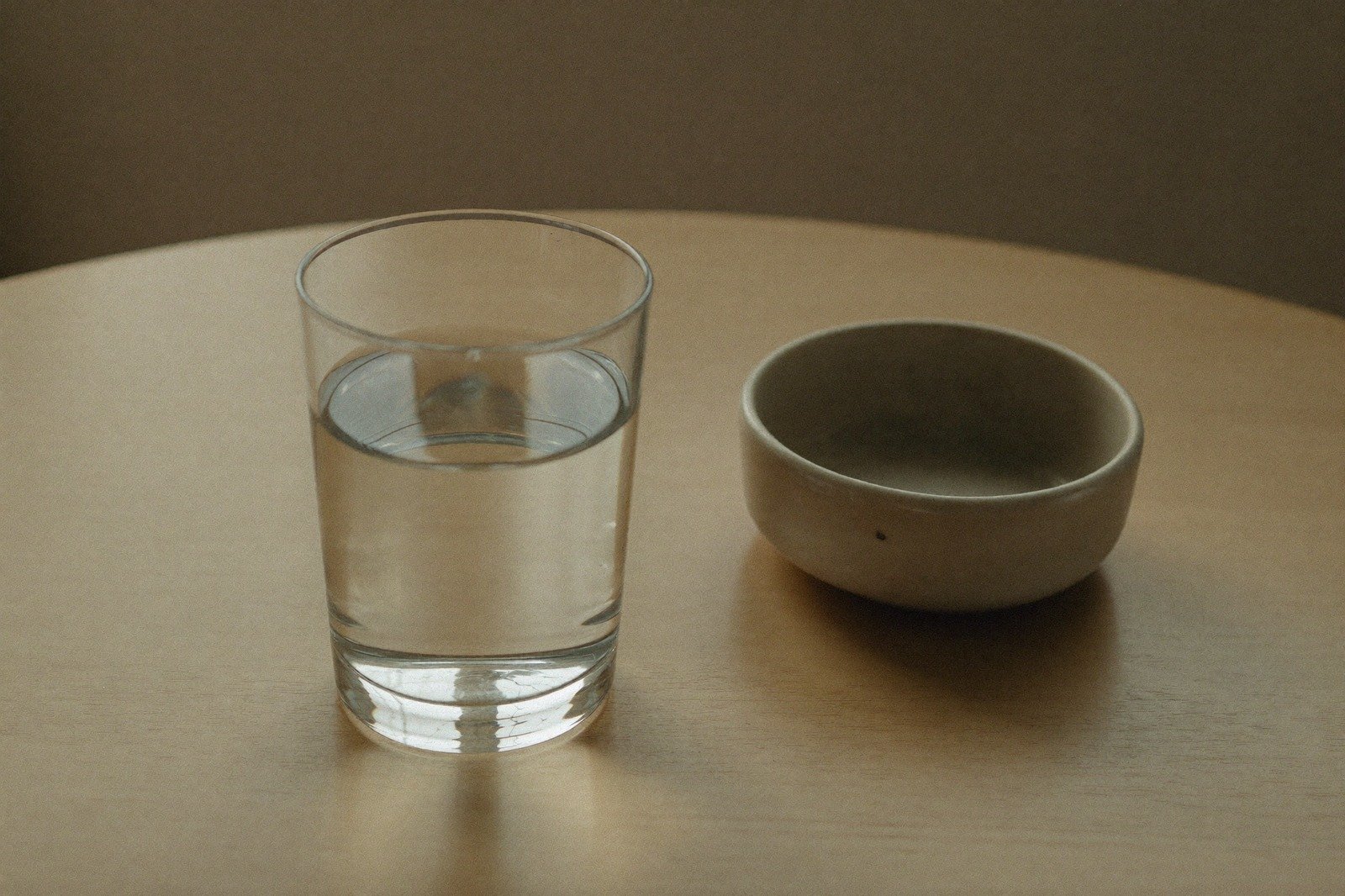 Vaso de vidrio con agua sobre una mesa de madera clara junto a un tazón pequeño de cerámica