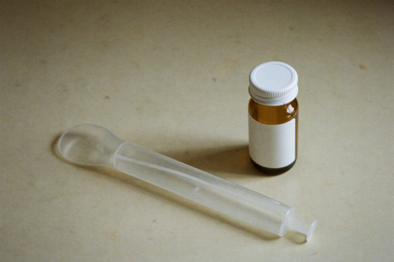 Jeringa oral de plástico junto a un frasco de medicamento sobre una superficie clara
