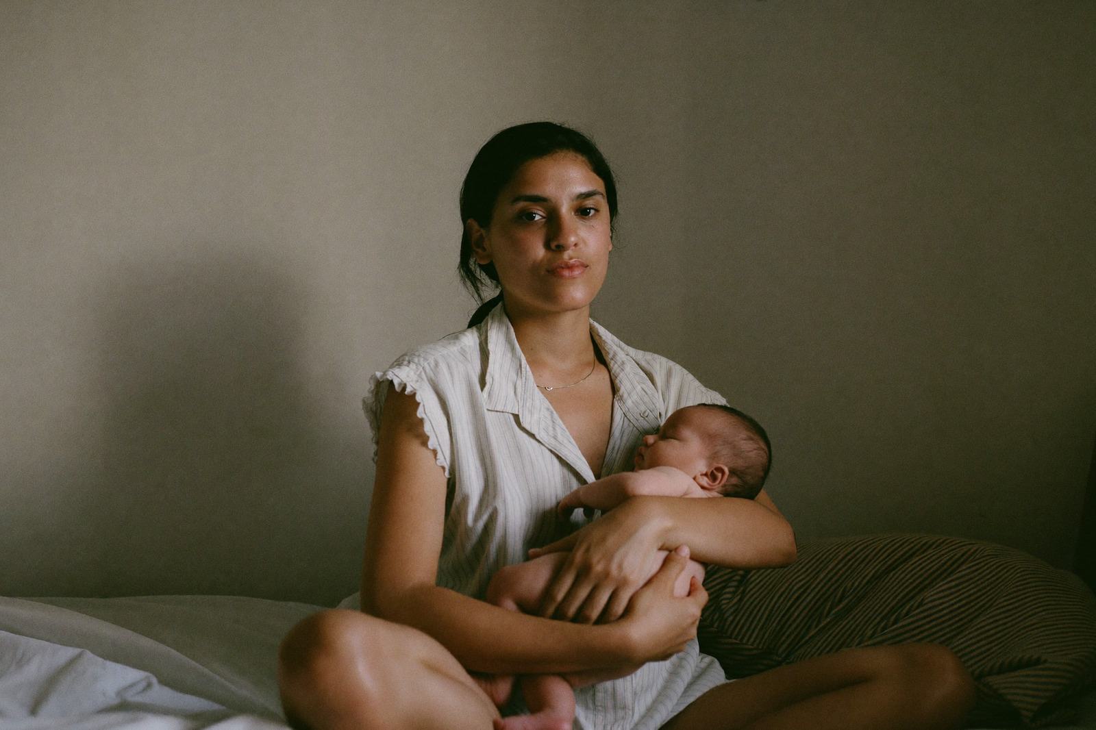 Recién nacido dormido en brazos de su mamá, con la luz de la ventana sobre la cara