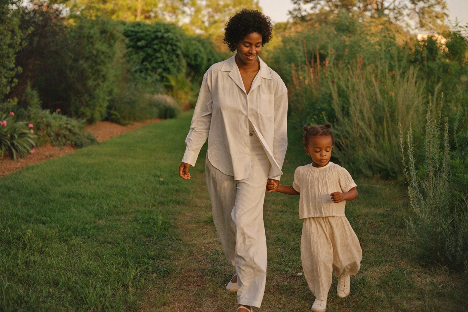 Mamá y su hija caminando juntas por un jardín al atardecer