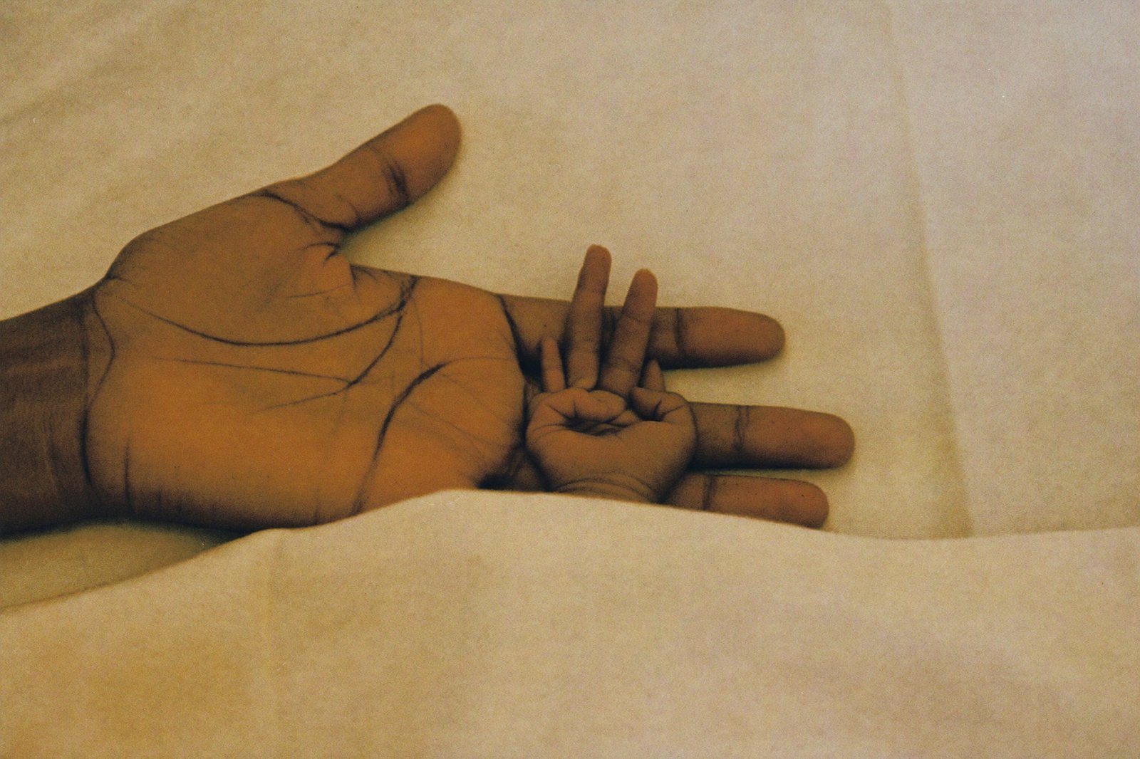 Mano de un adulto sosteniendo la manita de un bebé prematuro sobre una manta tejida clara