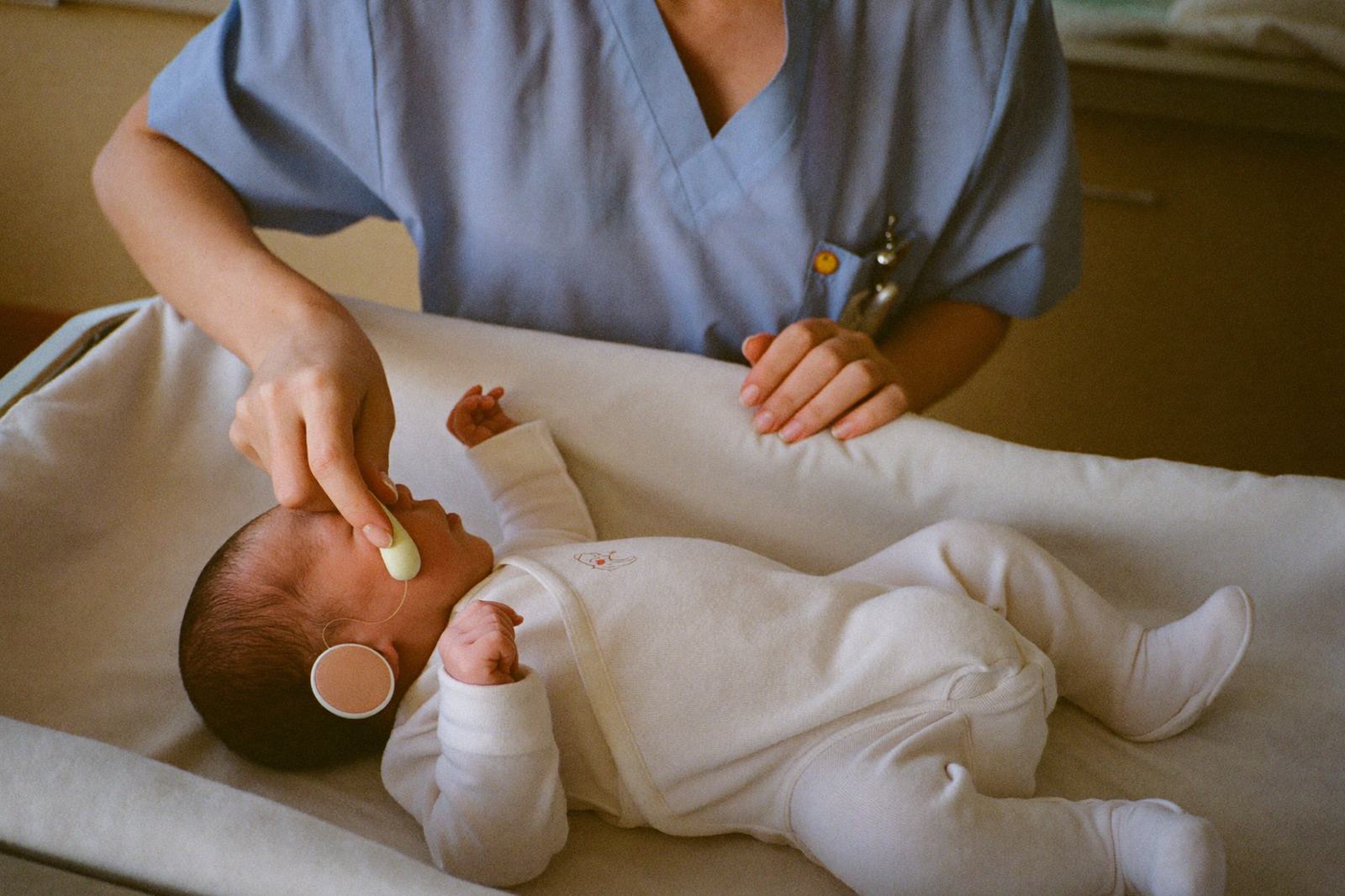 Personal de salud colocando un pequeño auricular en la oreja de un recién nacido acostado en una cuna del hospital