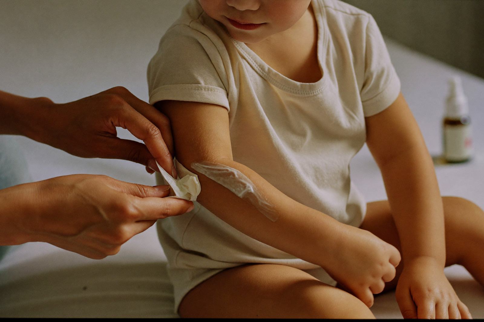 Un adulto aplica loción con un algodón en el brazo de un niño, con el frasco al fondo