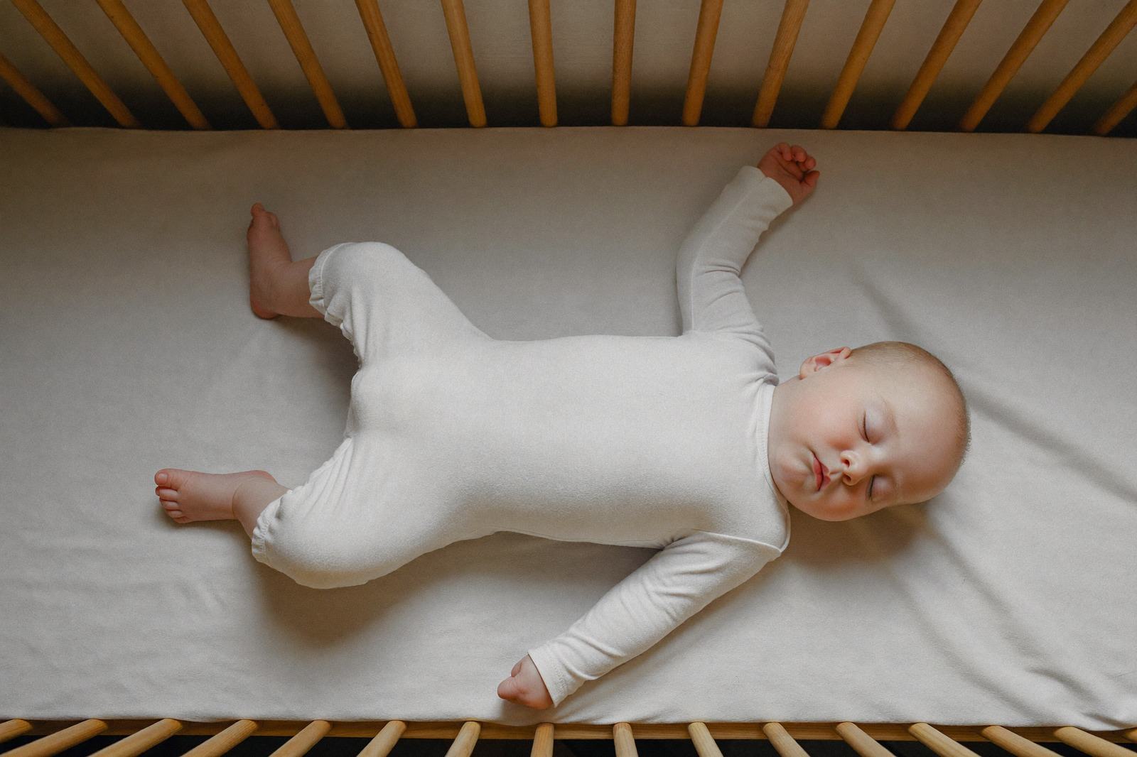 Bebé dormido boca arriba en una cuna de madera, con una sábana ajustada y nada más alrededor