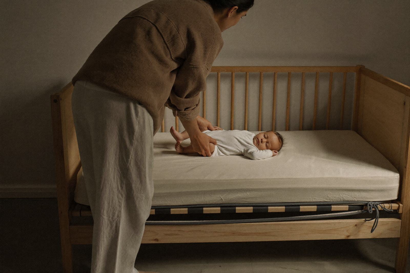 Manos de un adulto bajando a un bebé dormido a la cuna, con la cadera tocando el colchón antes que la cabeza