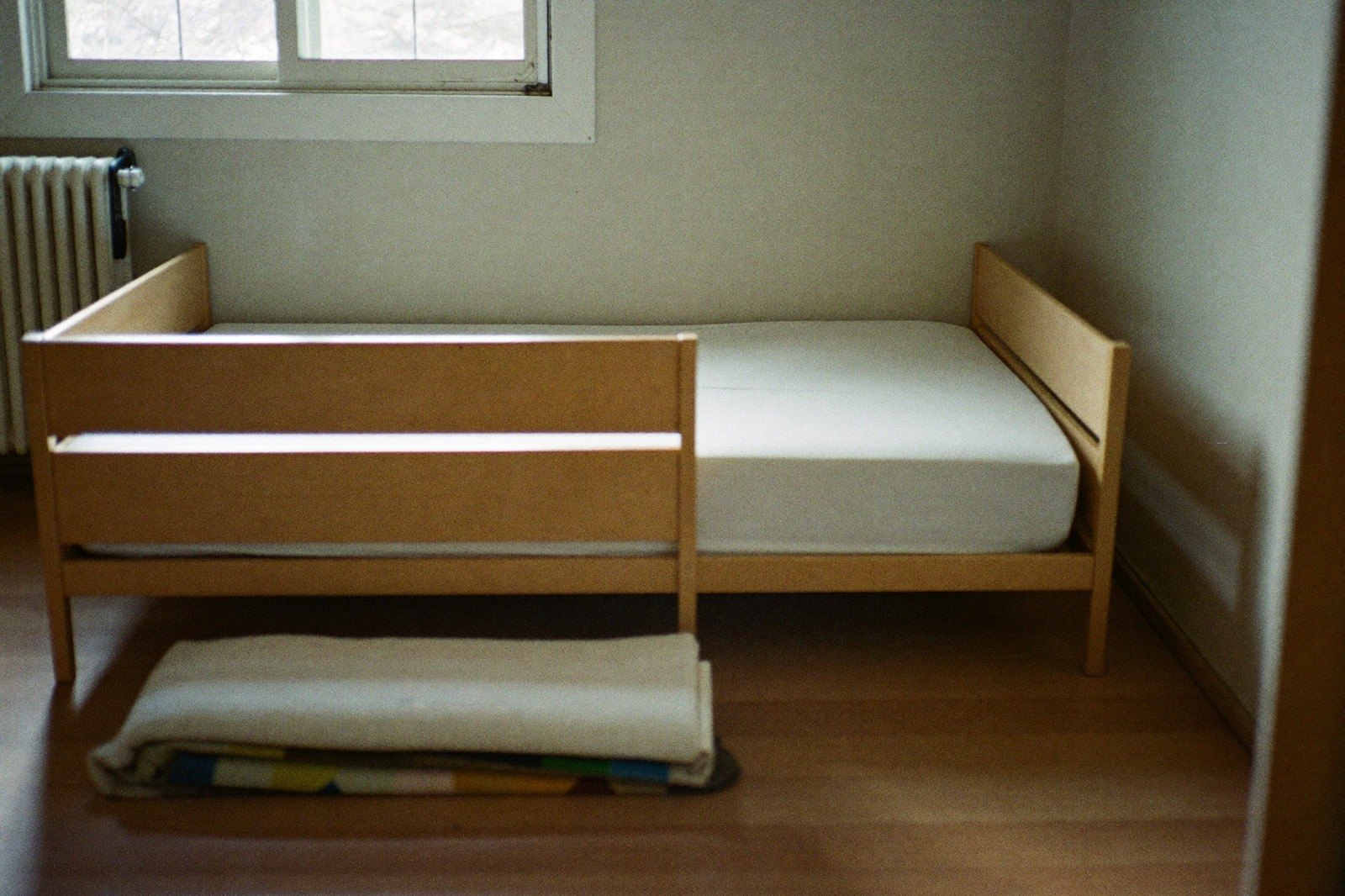 Cama baja de niño con un barandal en el costado, en una habitación ordenada con luz de mañana