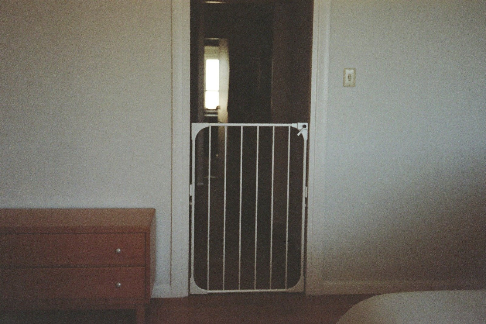 Puerta de un cuarto infantil con una reja de seguridad colocada y una cómoda baja sujeta a la pared