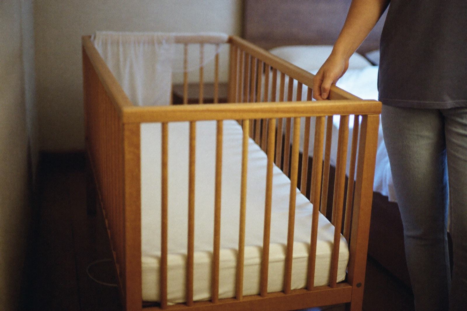 Una cuna de madera colocada junto a la cama de los papás, a la misma altura, en una recámara con luz de día