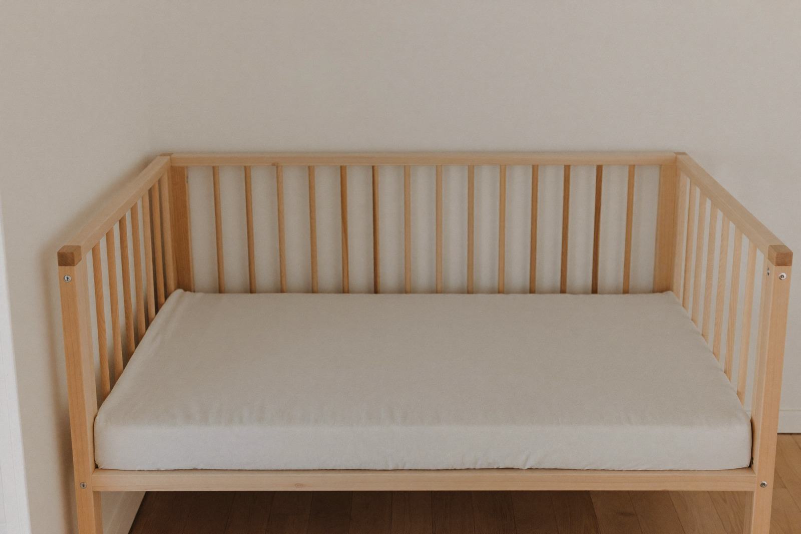 Cuna de madera vacía con una sábana ajustada blanca sobre el colchón, iluminada por luz natural
