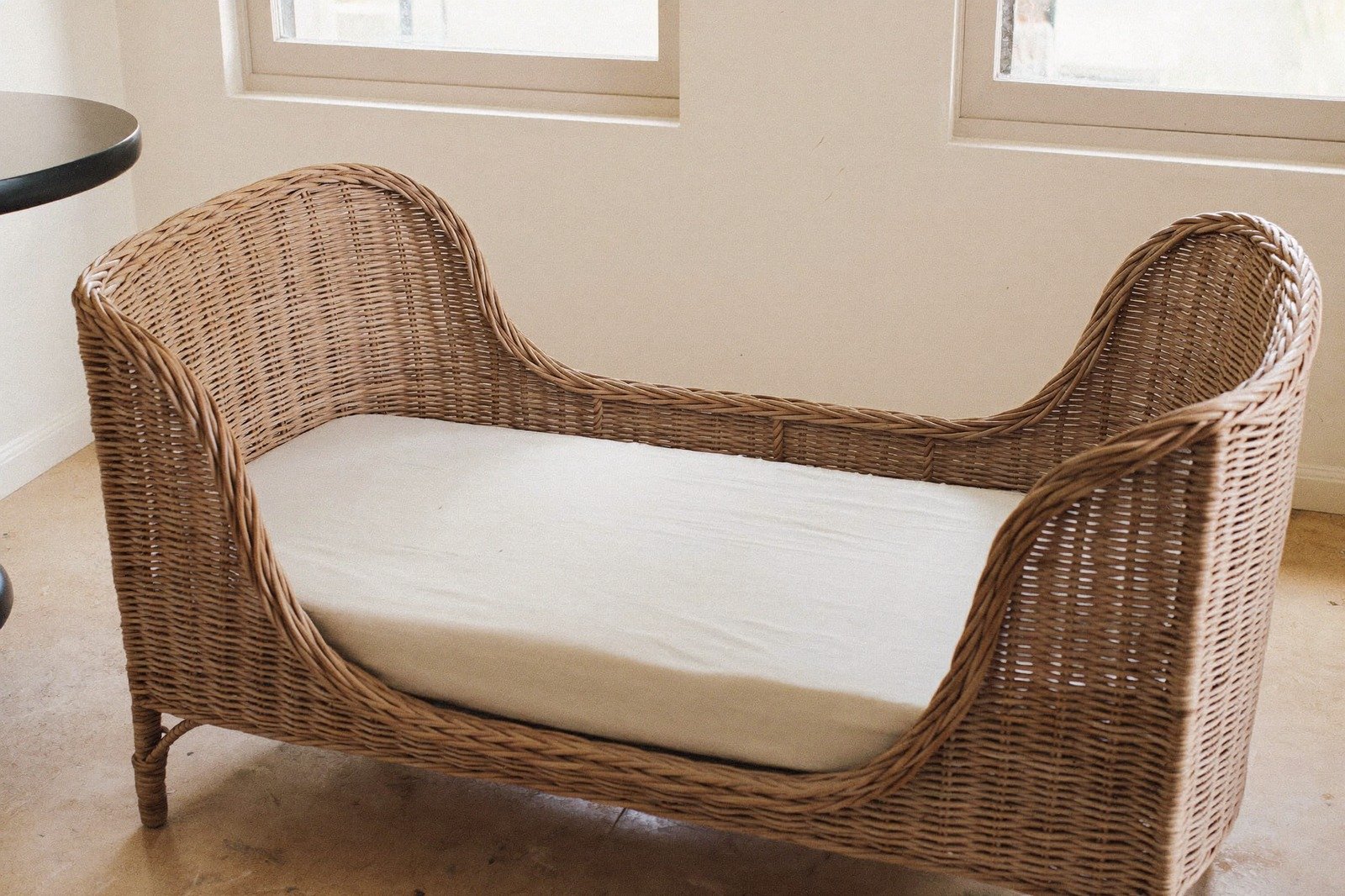 Moisés de mimbre con sábana ajustada blanca en una habitación luminosa, sin objetos adentro