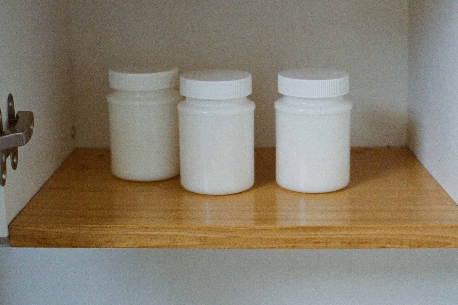 Frascos blancos sin etiqueta guardados en la repisa alta de una alacena de cocina